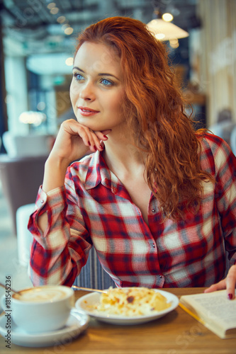 Tableau sur toile Red haired woman reading book  in cafe. City break  concept