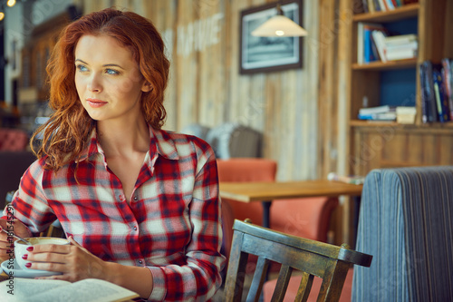 Red haired woman reading book in cafe. City break concept
