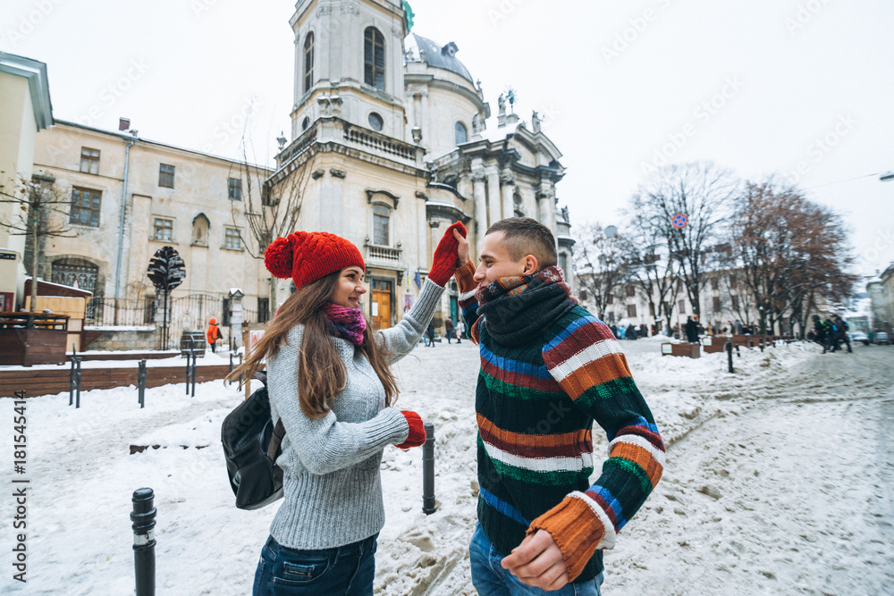 Wide street portrait of young happy smiling couple dressed in knitted clothes on the old architecture background in winter