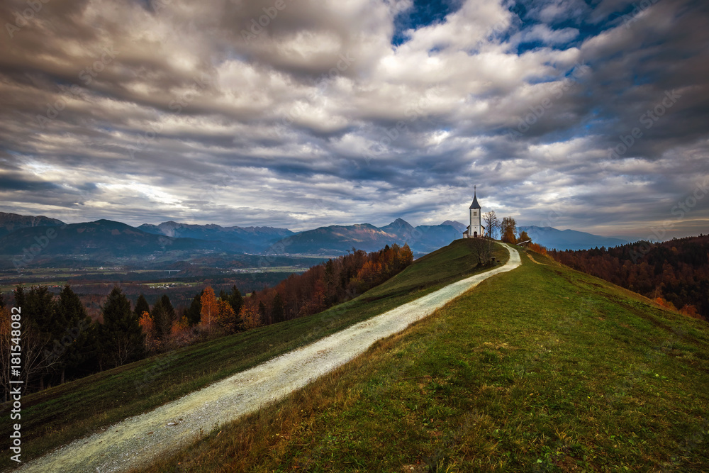 Jamnik, Slovenia - The beautiful church of St. Primoz in Slovenia near Jamnik with beautiful clouds and Julian Alps at background