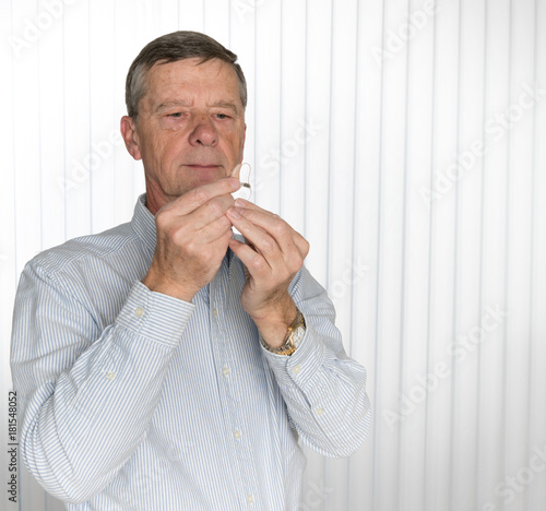 Close up of a tiny modern hearing aid with senior man