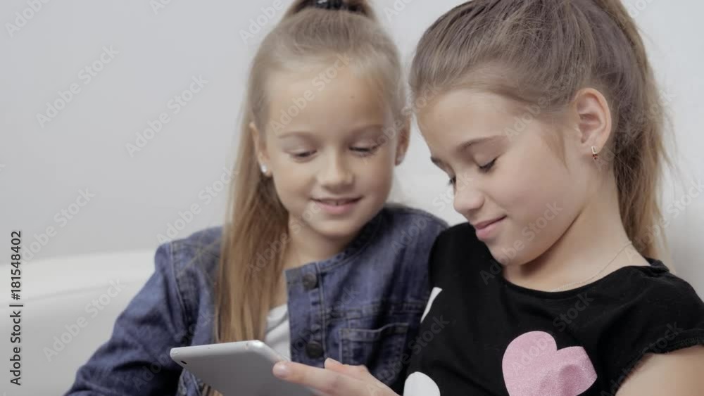 Close up portrait of two smiling girls lying on couch and using tablet, pretty happy little students Close up portrait of two smiling girls lying on couch and using tablet, pretty happy little students