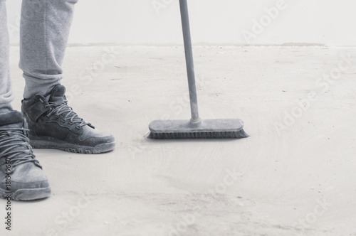 people, housework, cleaning and housekeeping concept - close up of legs with broom sweeping floor