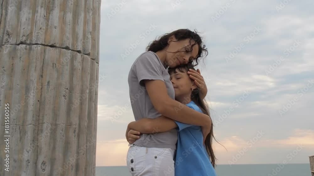 A woman is hugging a child against the sea. The daughter hugs her mother. A woman is hugging a child against the sea. The daughter hugs her mother.