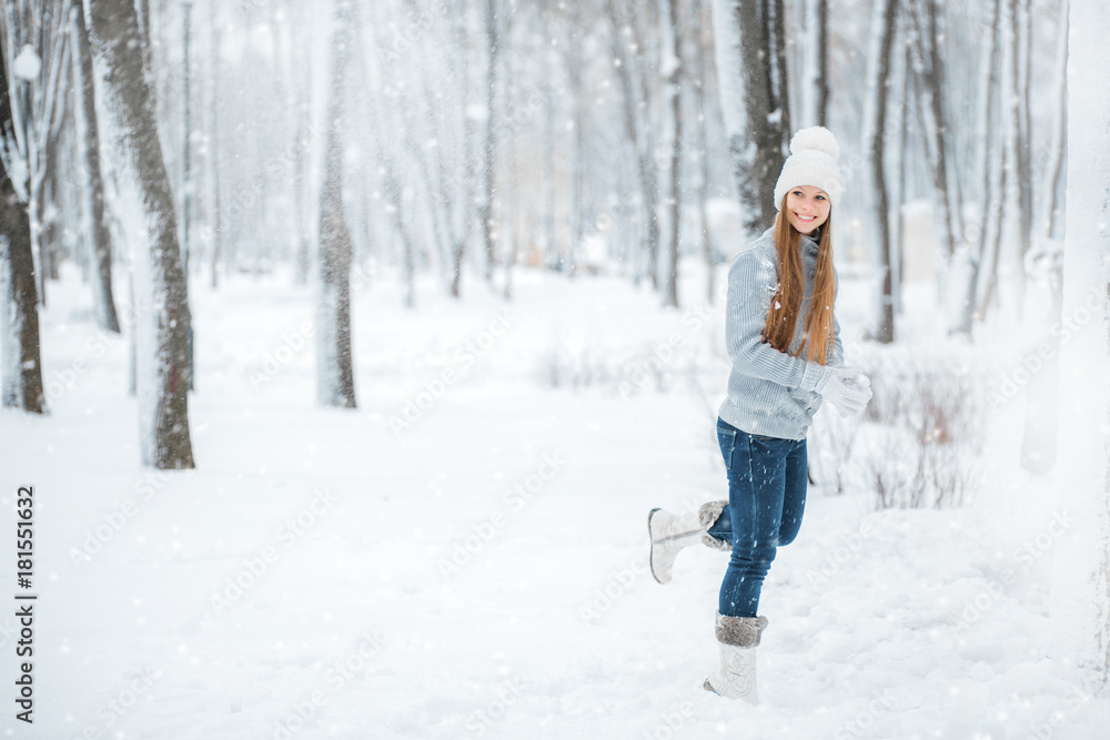 Outdoor close-up portrait of young beautiful happy smiling girl, wearing stylish knitted winter hat and gloves. A girl running through the snow-covered forest.