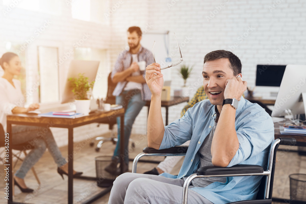 Disabled person in the wheelchair works in the office. He talks on smartphone. Disabled person in the wheelchair works in the office. He talks on smartphone.