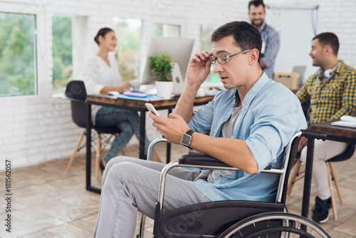 Disabled person in the wheelchair works in the office. He talks on smartphone.
