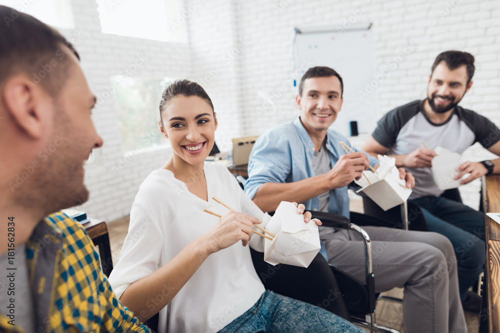 A group of young people and man in wheelchair are talking and eating Thai food. They are in a bright office A group of young people and man in wheelchair are talking and eating Thai food. They are in a bright office
