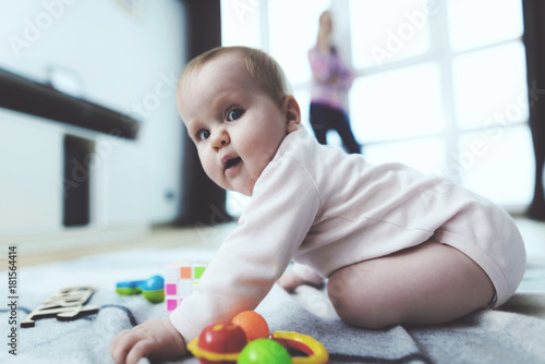 The baby is unattended. While the woman is talking on the phone, her child crawls on the floor and is played.
