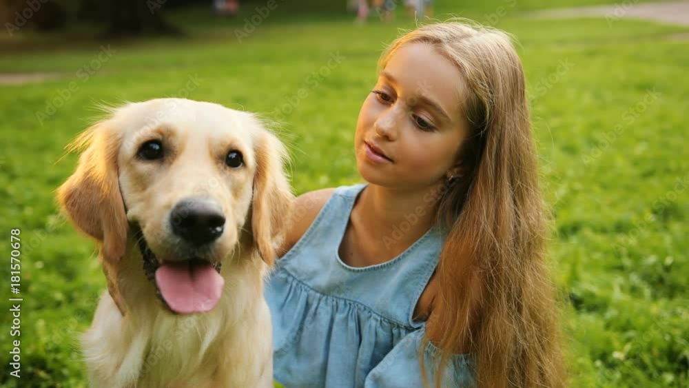 Close up. Portrait of a handsome long-haired teen girl playing with her labrador dog and caressing it. Then - looking into the camera and smiling. Park background Close up. Portrait of a handsome long-haired teen girl playing with her labrador dog and caressing it. Then - looking into the camera and smiling. Park background