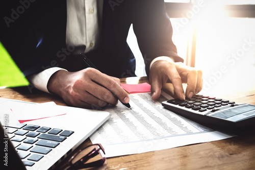 Принти на полотні Hand right of businessman holding a pen  pointing tax paper and left hand using calculator  accountant analyze income & budget, post it note and laptop computer on wooden desk at office