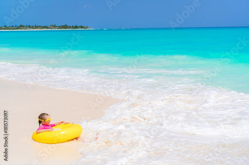 Happy little girl with inflatable rubber circle having fun on the beach in yhe shallow water