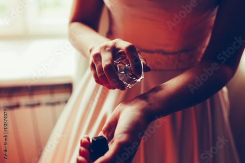 Girl in white expensive dress, spray expensive perfume on his hand, preparing to release against the window of the hotel. Woman spraying perfume on wrist, close-up. Vintage tonted photo. photo