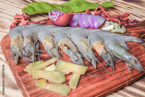 Fresh giant prawn on cutting board with onion, garlic, petai, key lime, chilies, lemongrass, and ginger.
