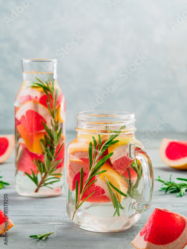 infused detox water with grapefruit and rosemary in mason jar and glass bottle on gray wooden table. diet healthy eating and weight loss concept, copy space for text