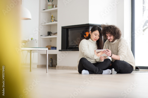 multiethnic couple using tablet computer in front of fireplace