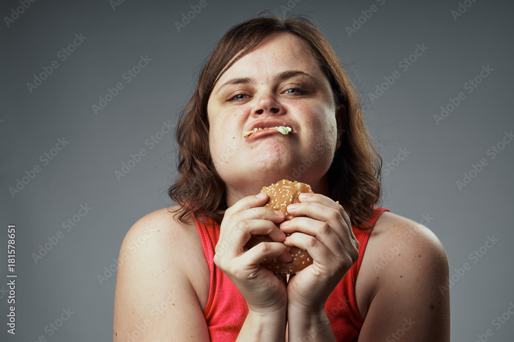 Fat, a woman on a gray background eating a hamburger, fast food,diet