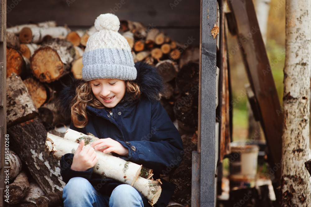 happy child girl picking firewood from shed in winter or autumn