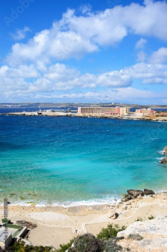 Rocky coastline with hotels and ferry terminal to the rear, Paradise Bay, Malta.