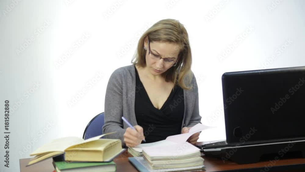 female teacher checks homework in classroom in front of laptop female teacher checks homework in classroom in front of laptop