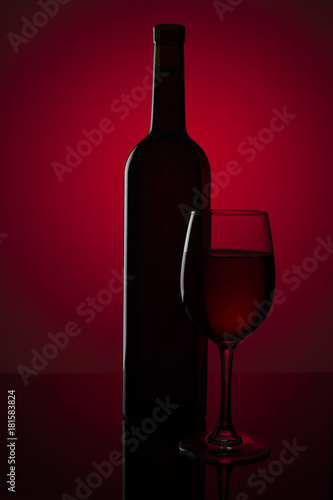 Bottle of red wine and a glass of wine on a red background