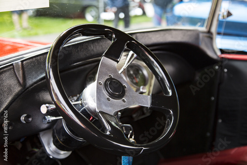 Isolated Interior View of Restored Tricked Out Vintage 50s Automobile Dashboard and Steering Wheel, Fabric Seats, with Out of Focus People and Cars in Background