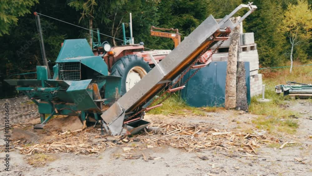 Small sawmill in the village. A tractor and a saw stand in the woods, alongside cut and packaged logs Small sawmill in the village. A tractor and a saw stand in the woods, alongside cut and packaged logs