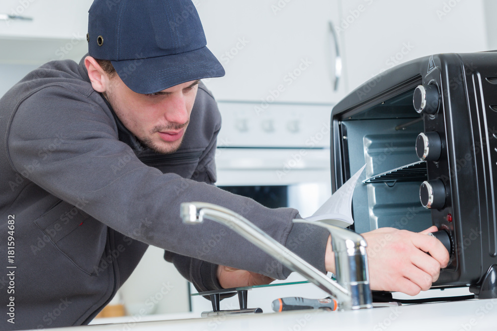 young repairman repairing oven with screwdriver in clients kitchen young repairman repairing oven with screwdriver in clients kitchen
