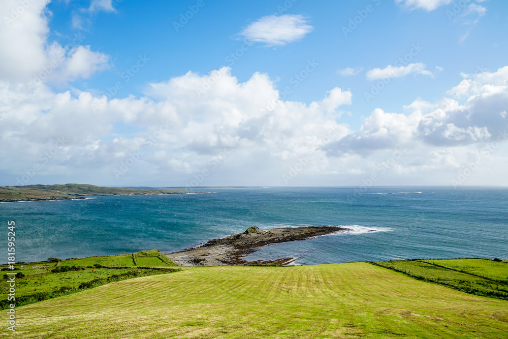 The beautiful green grasses of Ireland contrast well with the blue waters of the Atlantic along with the blue sky.