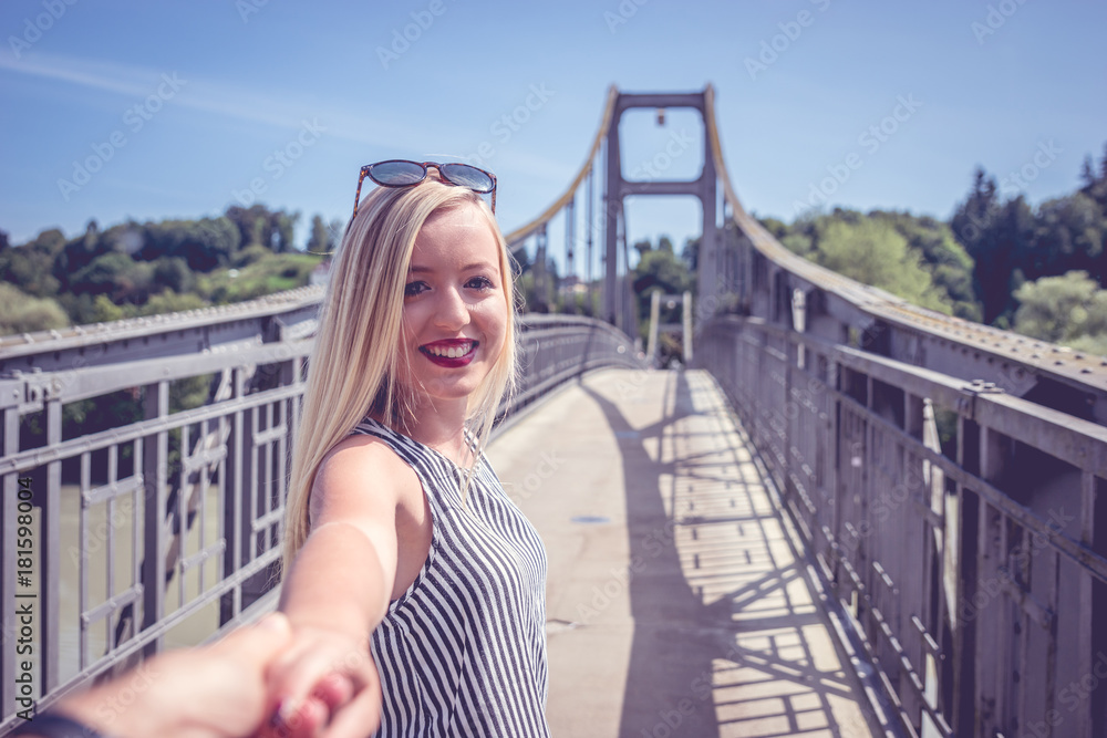 Junges hübsches Mädchen, zieht Ihren Freund an der Hand über eine Brücke und lächelt