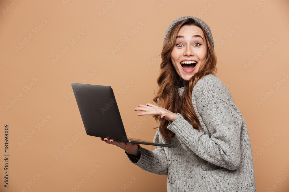 Naklejka premium Happy exited attractive girl in warm clothes holding laptop computer while looking at camera