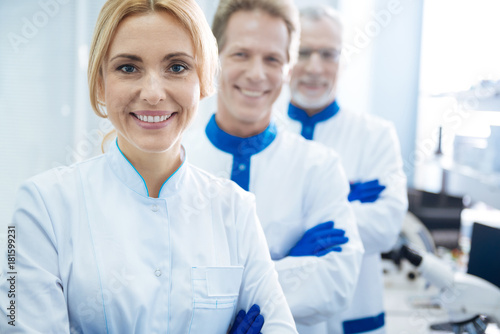 Gene lovers. Exuberant skilled experienced researchers smiling and wearing uniforms and standing one by one