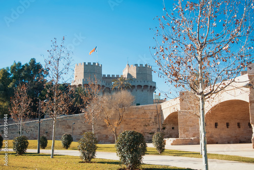 A view from Turia park gardens to  Serranos Gate with a flag, famous Valencian Towers, part of the ancient city wall, and a roman bridge at the foreground on autumn winter sunny day. photo