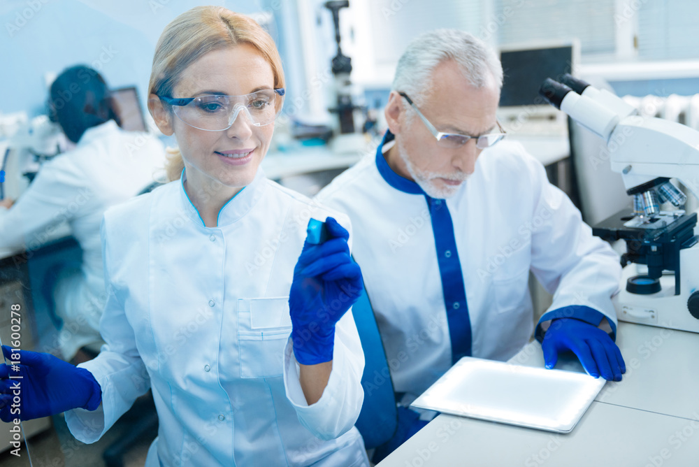 Preparation for analysis. Good-looking happy smiling woman scientist wearing a uniform and glasses and holding a marker while being in the lab Preparation for analysis. Good-looking happy smiling woman scientist wearing a uniform and glasses and holding a marker while being in the lab