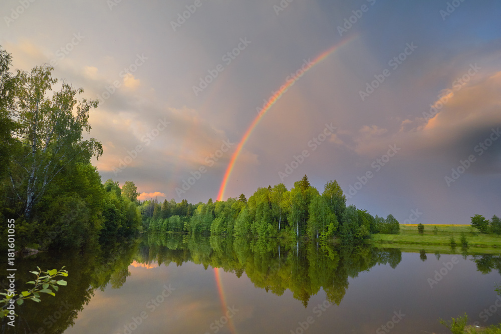 Rainbow over calm water of a forest lake. Beautiful clouds in the evening sky. Rainbow over calm water of a forest lake. Beautiful clouds in the evening sky.
