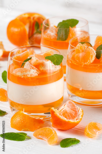 Creamy panna cotta with orange jelly in beautiful glasses, fresh ripe mandarin, on white wooden background. Delicious Italian dessert. Closeup photography. Selective focus.