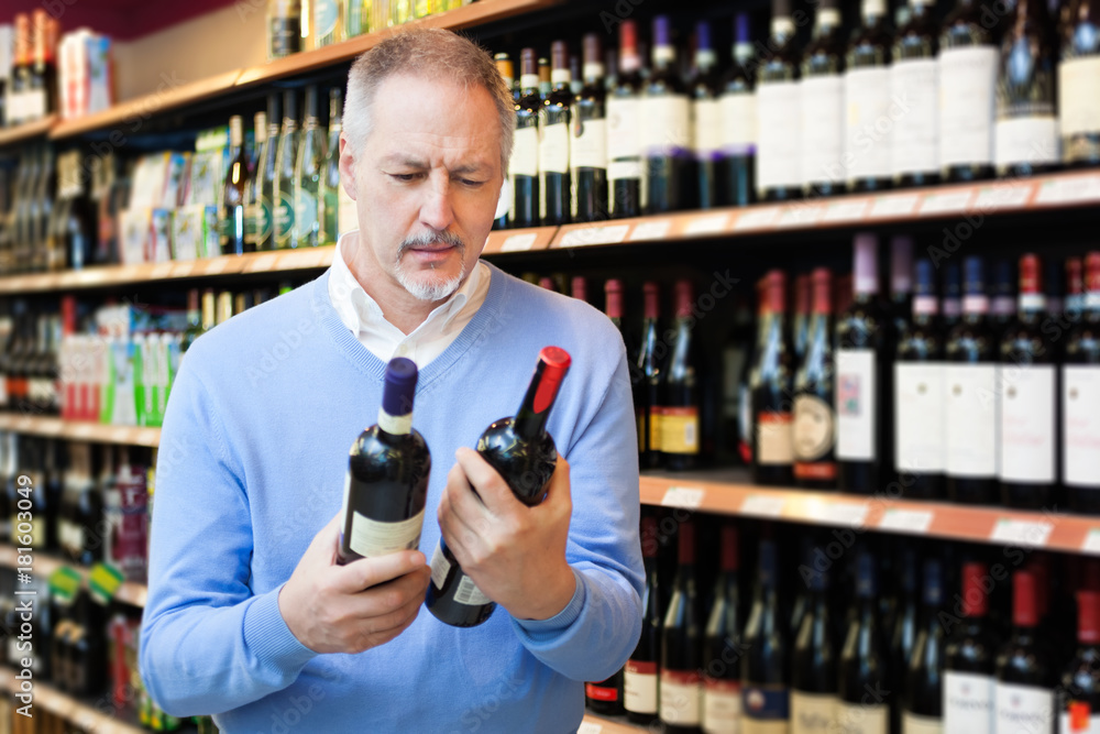 Man in a supermarket choosing the best wine