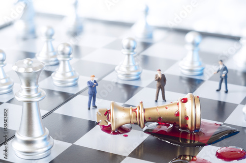 Conceptual photo with chess pieces, toy businessmen and blood on a chessboard. Business, law or political concept, which could represent war of corporations, geopolitical situation and so on.