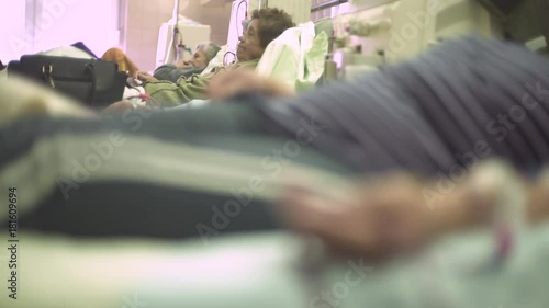 Mature female patients lying in the beds during hemodialysis treatment, focus change from portrait of elderly woman to hand during blood flows through the tube injected in vein, macro shot, real scene photo