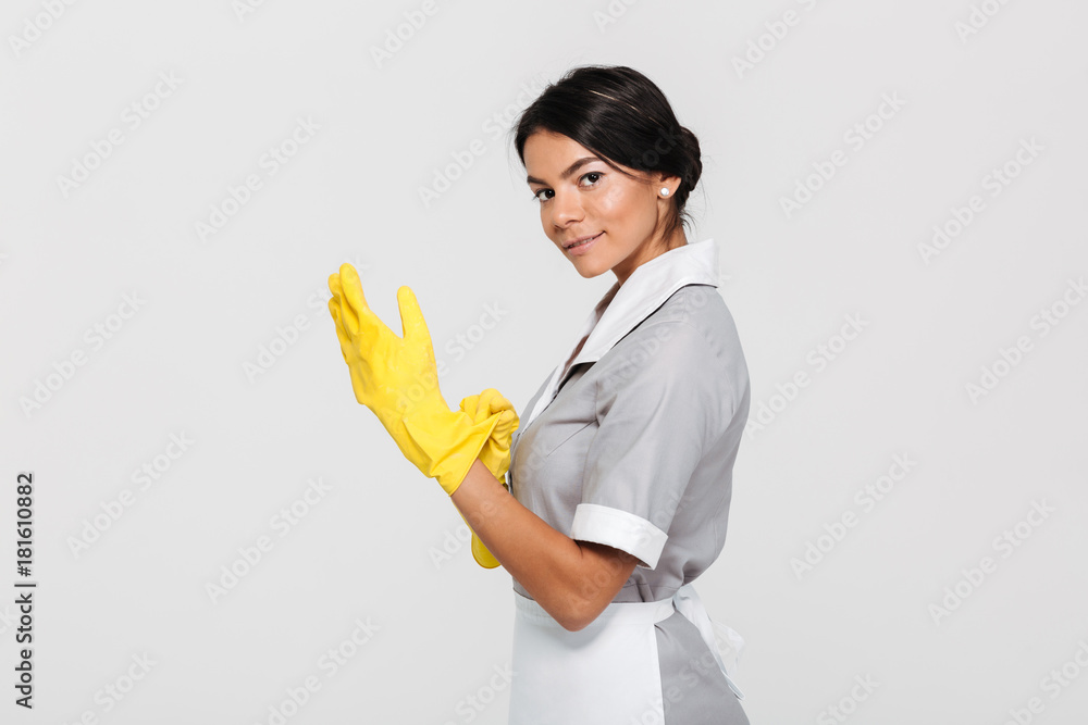 Portrait of young cheerful housekeeper wearing yellow rubber gloves while standing and looking at camera Portrait of young cheerful housekeeper wearing yellow rubber gloves while standing and looking at camera