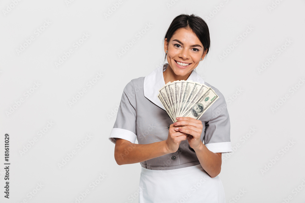 Portrait of young attractive female maid holding bunch of money and looking at camera Portrait of young attractive female maid holding bunch of money and looking at camera