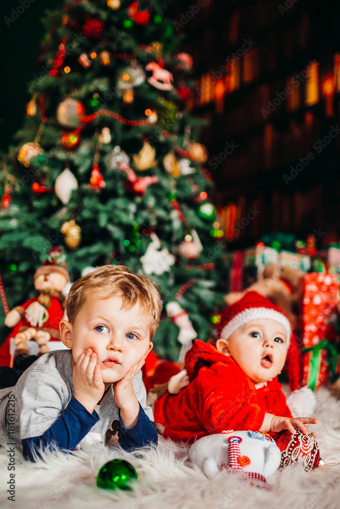 Two pretty little boys lie on fluffy carpet before a Christmas tree Two pretty little boys lie on fluffy carpet before a Christmas tree