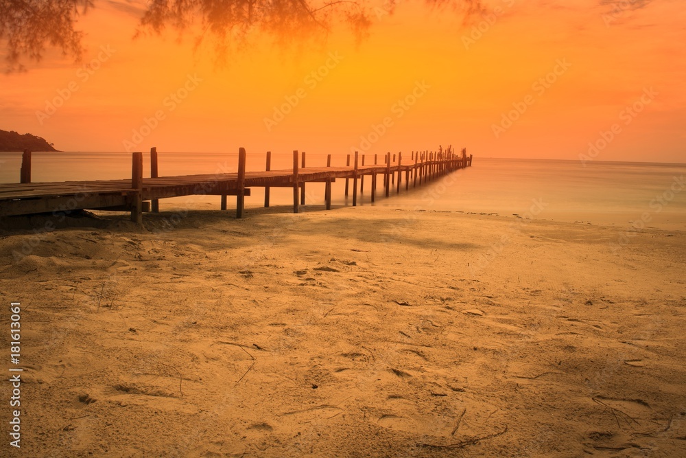 Old wooden bridge extends into the sea (fill with orange light).