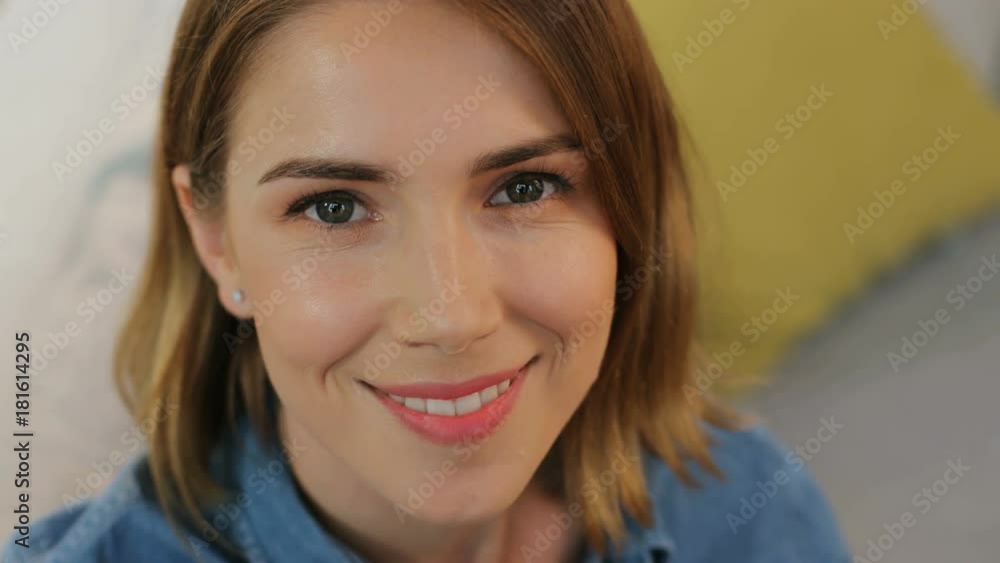 Attractive young woman smiling at the camera while relaxing on the sofa in the living room. Top view. Close up. Attractive young woman smiling at the camera while relaxing on the sofa in the living room. Top view. Close up.