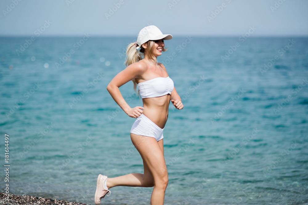 Beautiful young blonde woman in white sportswear is running on beach