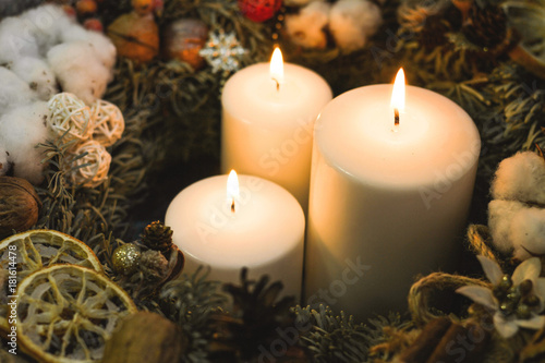 White burning christmas candles in a christmas wreath decorated with lemons and pinecones