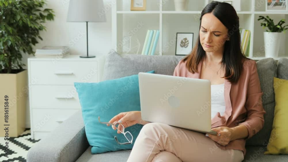 Portrait of attractive business woman finishing her work on the laptop at home and taking off glasses while sitting on the sofa. Portrait of attractive business woman finishing her work on the laptop at home and taking off glasses while sitting on the sofa.