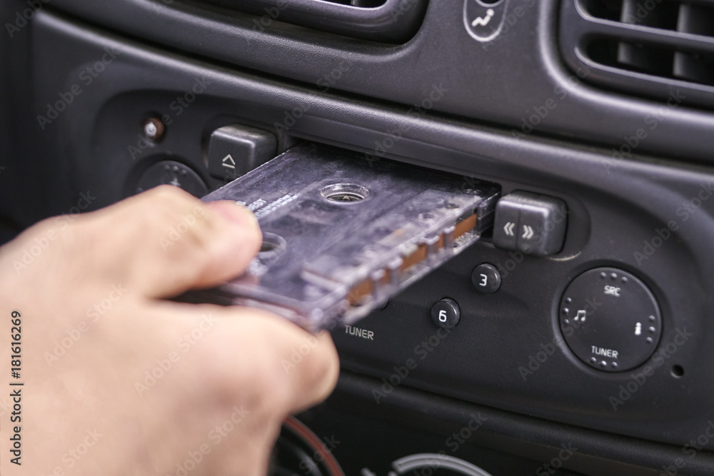 Fototapeta premium Male hand inserting a music cassette in old car tape player
