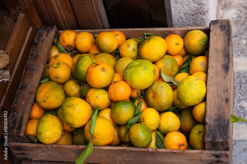 Wooden basket of greenish mandarin oranges (tangerins) with green leaves for sale