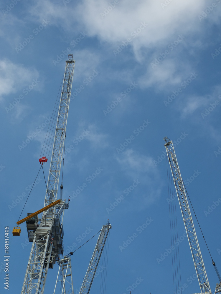 white construction cranes on a building site against a cloudy blue sky